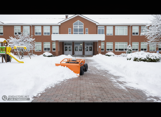 Orange remote control mower clearing a snow-covered brick path in front of a large brick school building on a cloudy winter d