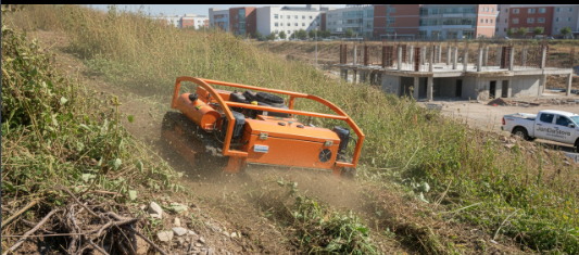 Orange remote control crawler mower clearing dense brush on a steep, overgrown slope near construction.