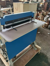 Blue and grey industrial electric punching machine with a wide work surface, showing the punching mechanism and foot pedal.